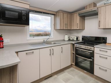 A kitchen with oven microwave toaster kettle sink and countertop with a window showing a landscape at Gwent 74 in Borth