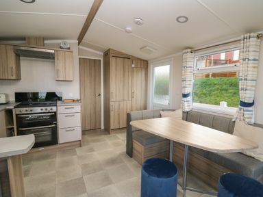 A kitchen and dining area with wooden cabinets a stove a corner bench seating a wooden table and blue stools at Gwent 74 in Borth