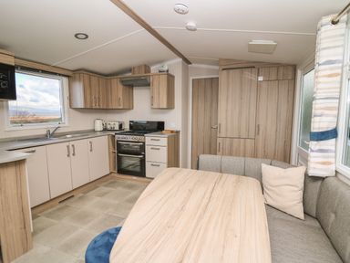 A kitchen and dining area with wooden cabinets, a stove, a sink, a table, and corner seating at Gwent 74 in Borth