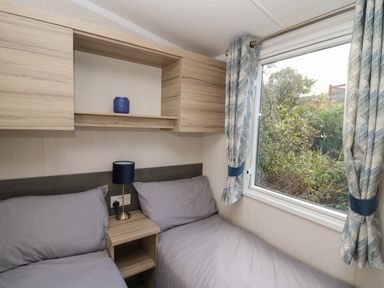 A bedroom with two single beds separated by a wooden bedside table with a lamp and a window with curtains at Gwent 74 in Borth