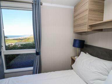 A bedroom with a bed white pillows a blue lamp wooden cabinets and a window with a view of the sea at Gwent 74 in Borth