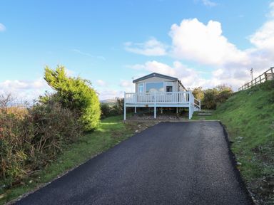 A mobile home with a white deck at the top of a driveway with grass and bushes on either side at Gwent 74 in Borth