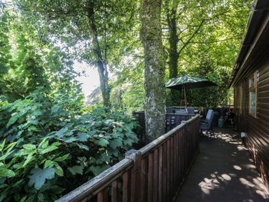 An outdoor area with a table and chairs under an umbrella at Treetops Beech Hill 13, Fallbarrow Park near Bowness-On-Windermere