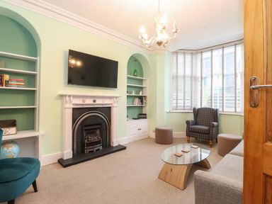 A living room with a fireplace a wall mounted tv a glass coffee table a sofa an armchair and bay window blinds at Blencathra in Keswick