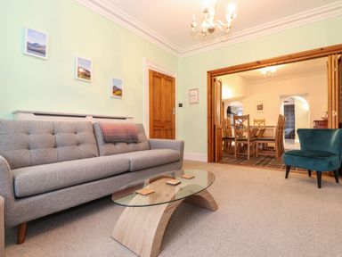 A living room with a gray sofa a glass coffee table and a blue armchair with a dining area visible through wooden sliding doors at Blencathra Keswick
