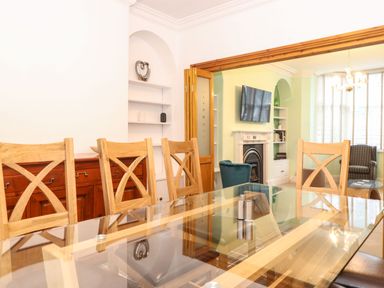 A dining area with wooden chairs and glass table facing a living room with a TV above fireplace at Blencathra in Keswick