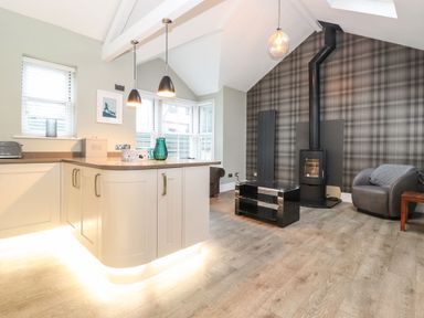 A kitchen and living area with a wood stove and a gray chair at Blencathra in Keswick