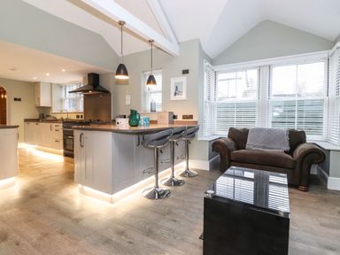 A kitchen area with an island and bar stools next to a sitting area with a sofa and a glass coffee table at Blencathra in Keswick