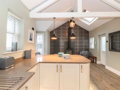 A kitchen with a central island and pendant lights next to a living area with a fireplace and armchair at Blencathra in Keswick