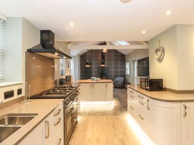 A kitchen with beige countertops, stove, sink, kitchen island, microwave, and a chair in the background at Blencathra in Keswick
