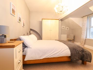 A bedroom with a bed pillows lamps a wardrobe chair and a window with curtains at Blencathra in Keswick