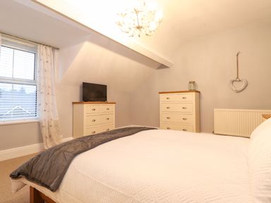A bedroom with a bed a tv on a dresser two dressers a window with blinds and curtains and a heart decoration on the wall at Blencathra in Keswick
