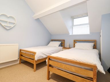 A bedroom with two wooden single beds white bedding a small bedside table under a window with blinds and a heart-shaped wall shelf at Blencathra in Keswick