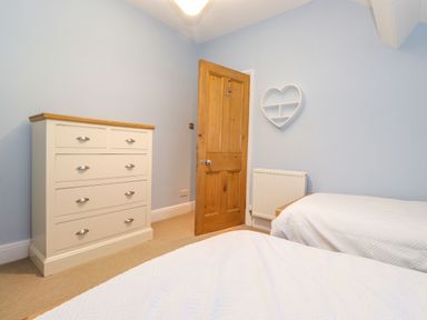 A bedroom with two beds a white chest of drawers a wooden door and a heart shaped wall shelf at Blencathra in Keswick
