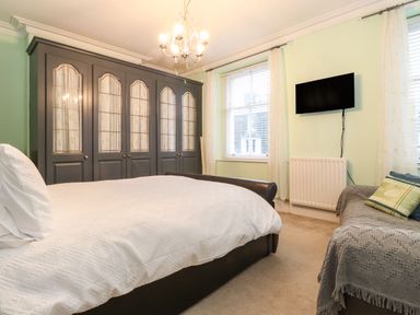 A bedroom with a large bed white bedding gray wardrobe a wall-mounted TV and a sofa covered with a blanket at Blencathra in Keswick