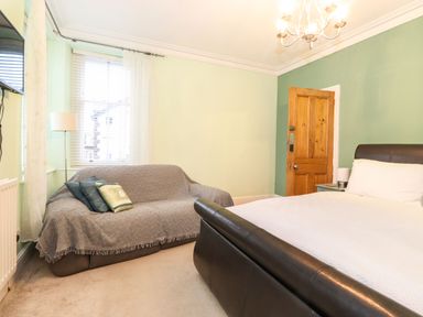 A bedroom with a bed a sofa with cushions a wooden door and a window at Blencathra in Keswick