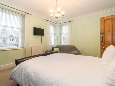 A bedroom with a bed a sofa wall-mounted TV and windows with blinds at Blencathra in Keswick