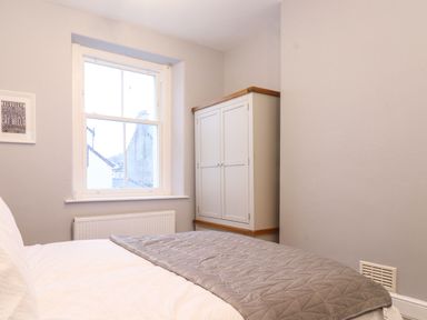 A bedroom with a bed grey quilt a white cabinet and a window showing buildings at Blencathra in Keswick