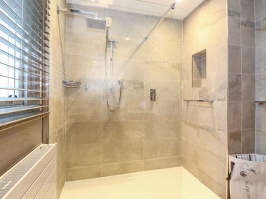 A walk-in shower with tiled walls a glass partition and a laundry basket in a bathroom at Blencathra in Keswick