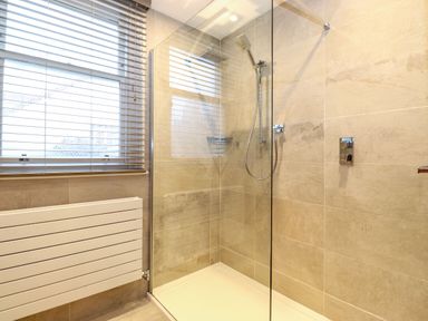 A bathroom with a glass shower enclosure a showerhead and a window with blinds at Blencathra in Keswick