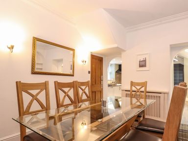 A dining room with a glass table and wooden chairs near a wooden door and mirror at Blencathra in Keswick