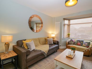 A living room with two sofas a coffee table a round mirror on the wall and windows with blinds at Birch House in Corsham