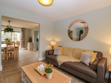 A living room with a brown sofa, cushions, a round mirror above, and a wooden coffee table with candles and flowers at Birch House in Corsham
