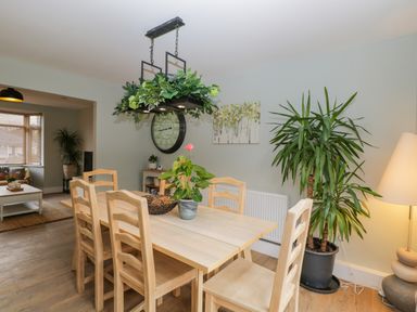 A dining room with a wooden table and six chairs with plants and a clock on the wall at Birch House in Corsham
