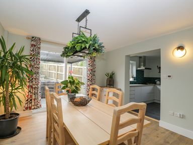 A dining room with a wooden table and chairs with plants and sliding glass doors next to a kitchen at Birch House in Corsham