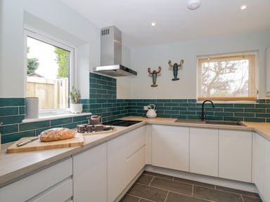 A modern kitchen with white cabinets green tiled backsplash and a wooden countertop at Birch House in Corsham