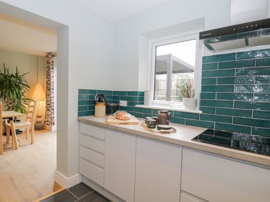 A kitchen counter with green tiled backsplash a window and a dining area visible through an opening at Birch House in Corsham