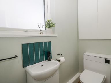 A small bathroom with a white sink and toilet and teal tiles behind the sink at Birch House in Corsham
