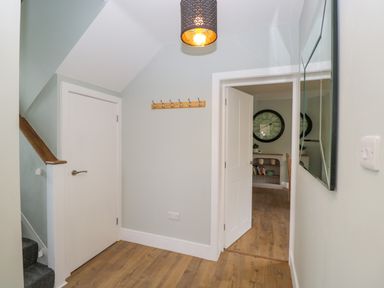A hallway with wooden floor a closed door under stairs a wall hook rack and an open door showing a room with a large clock at Birch House in Corsham
