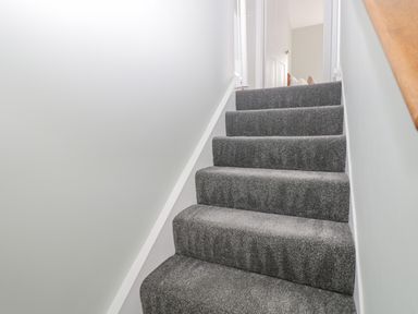 A staircase with gray carpet and white walls leading to an open door at Birch House in Corsham