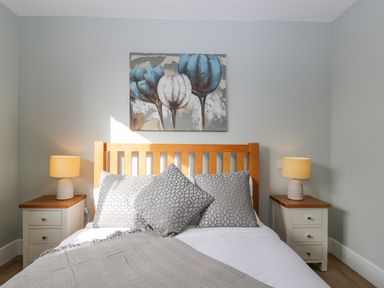 A bedroom with a wooden bed frame two bedside tables with lamps and floral artwork above the bed at Birch House in Corsham