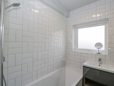 A bathroom with a bathtub shower combination tiled walls a window and a sink with a mirror at Birch House in Corsham