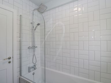 A bathroom with a bathtub shower combination featuring white patterned tiles and a glass shower screen at Birch House in Corsham