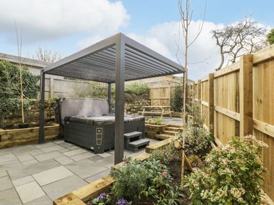 A garden with a hot tub under a pergola wooden fencing and a picnic table at Birch House in Corsham