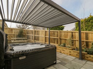 An outdoor area with a hot tub under a pergola and a wooden fence with plants at Birch House in Corsham