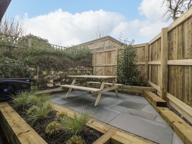 A fenced patio area with a wooden picnic table and raised garden beds with plants at Birch House in Corsham