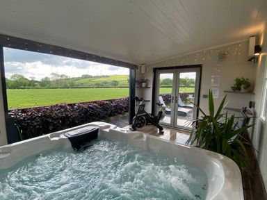 An indoor room with a hot tub spinning bike plants and double glass doors opening to an outdoor area with loungers and green fields at Ashlea in Launceston
