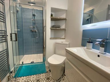 A bathroom with a glass shower, toilet, sink, shelves, and patterned floor tiles at Ashlea in Launceston