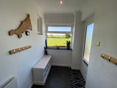 A small entryway with a window showing a green field a white bench with compartments a wooden wall map a clock and coat hooks at Ashlea in Launceston