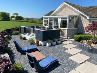 A garden patio with blue cushioned loungers a stone table and a raised dining area outside a house at Ashlea in Launceston