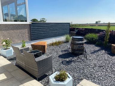 An outdoor patio area with a wicker loveseat, a wooden stump, potted plants, a wooden barrel table, and a metal bar stool at Ashlea in Launceston