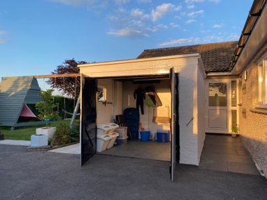 An open garage with hangers and containers next to a garden with a wooden play structure at Ashlea in Launceston