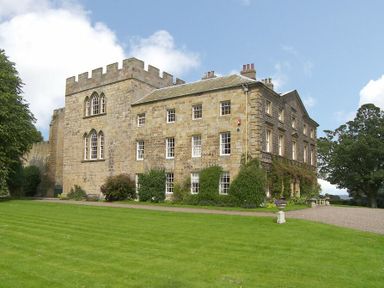 A large stone castle with battlements and multiple windows surrounded by a green lawn at Craster Tower Penthouse in Craster