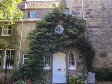 Front view of a stone house with a white door and plants growing around the door at Craster Tower Penthouse in Craster