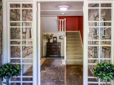 A stone entry hallway with carpeted stairs wooden chest and floral arrangement at Craster Tower Penthouse in Craster