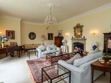 A living room with sofas, a grand piano, framed portraits on walls, a chandelier, a fireplace with a mirror above, and a patterned rug at Craster Tower Penthouse in Craster